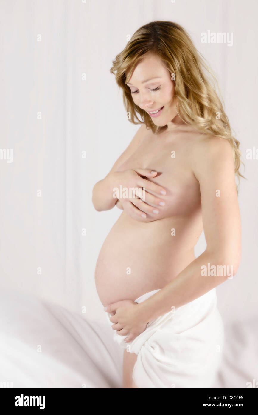 A sexy naked pregnant woman kneeling on the bed. Stock Photo by