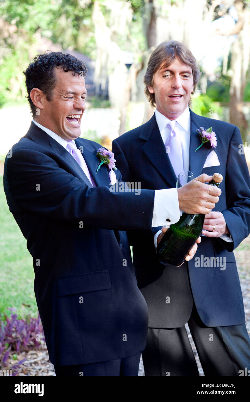 Handsome gay couple at their wedding, opening a bottle of champagne.  Stock Photo