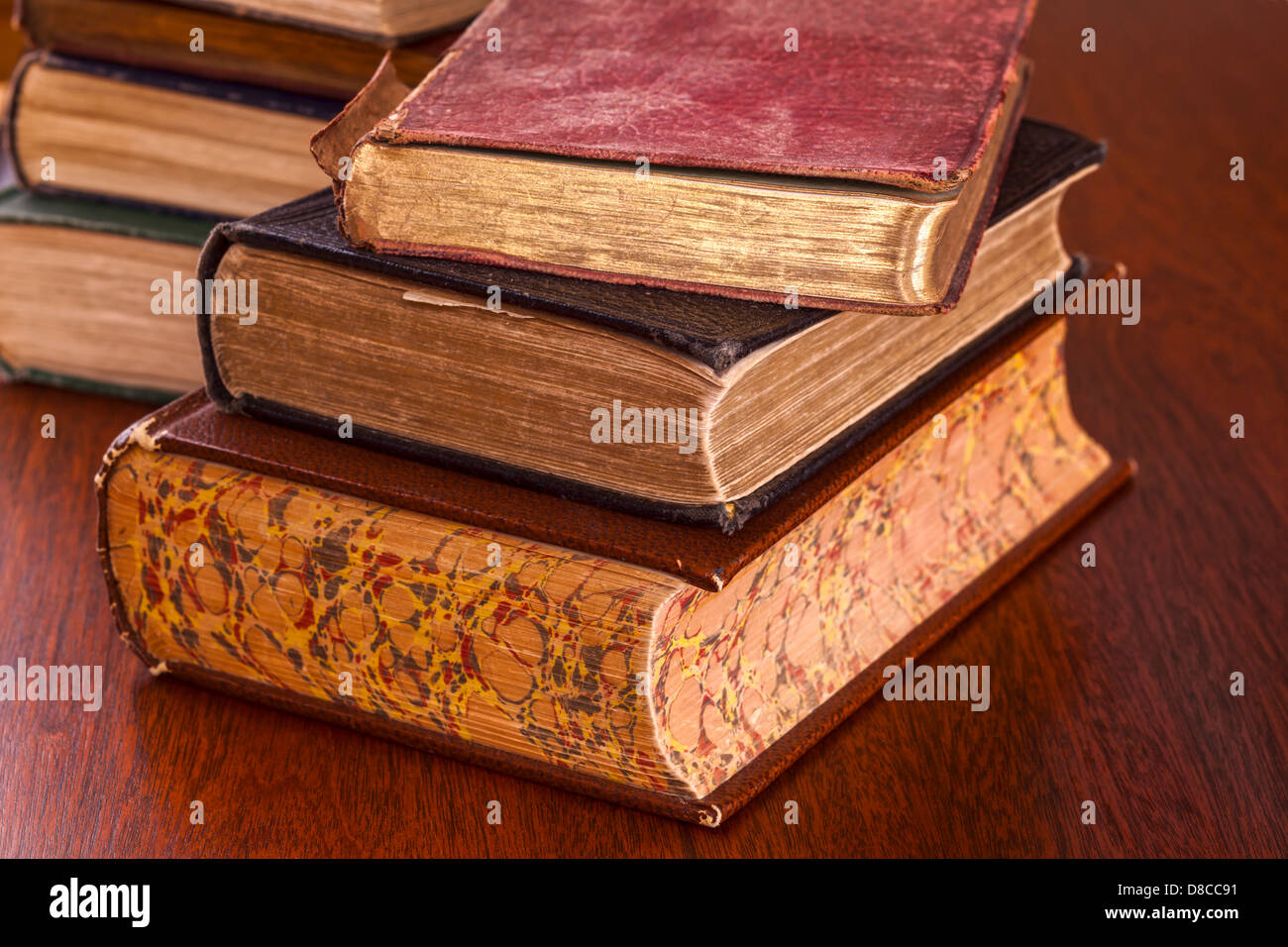 Old Books on Dark Wood Background - battered old books on a dark oak table, focus on foreground. Stock Photo