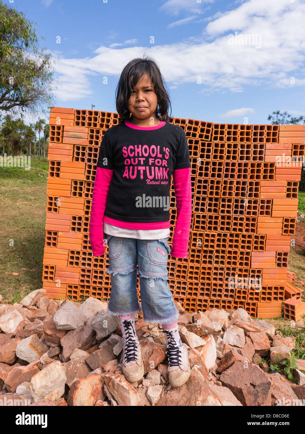 A young Hispanic girl stands in front of a pile of ceramic building blocks for home construction at a home building site. Stock Photo