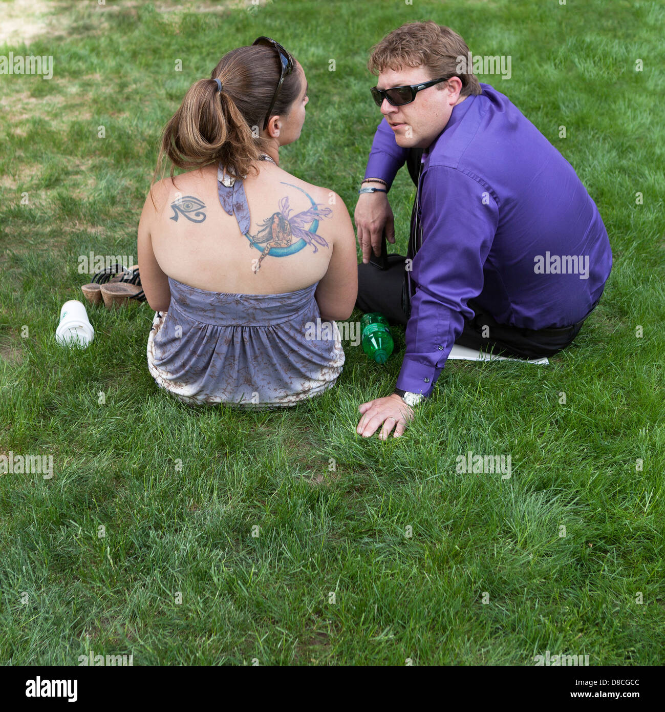 A woman with a large, colorful shoulder tattoo converses with a man on a lawn. Stock Photo