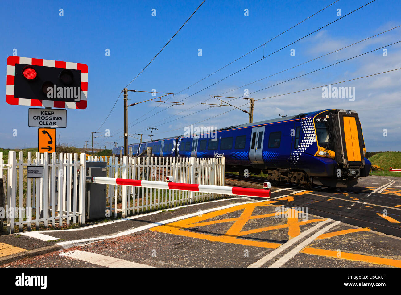 Electric train travelling across a controlled crossing, showing the traffic lights and control barrier, Ayrshire, Scotland, UK Stock Photo