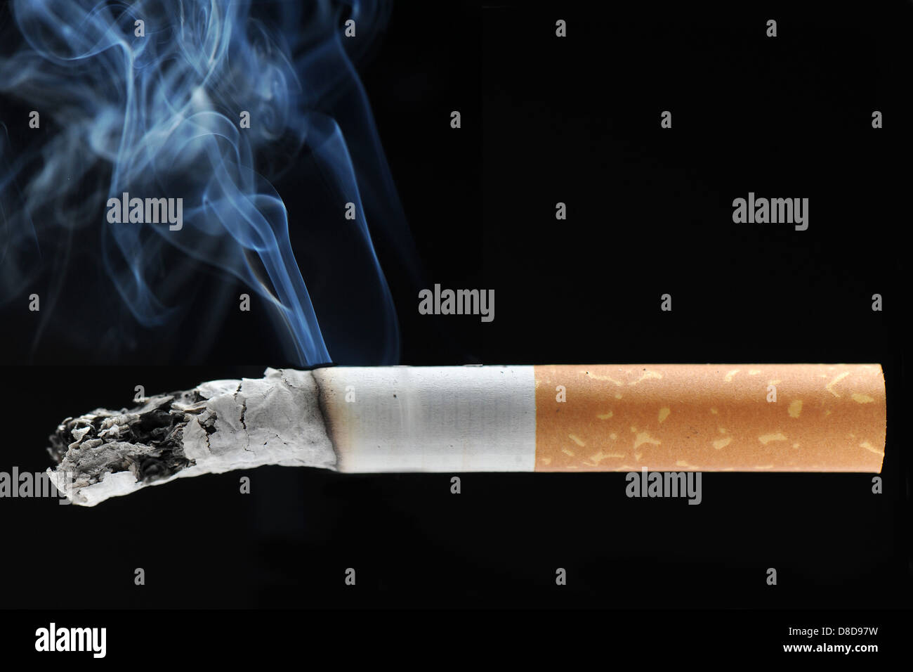 A burning cigarette with smoke against a black background Stock Photo