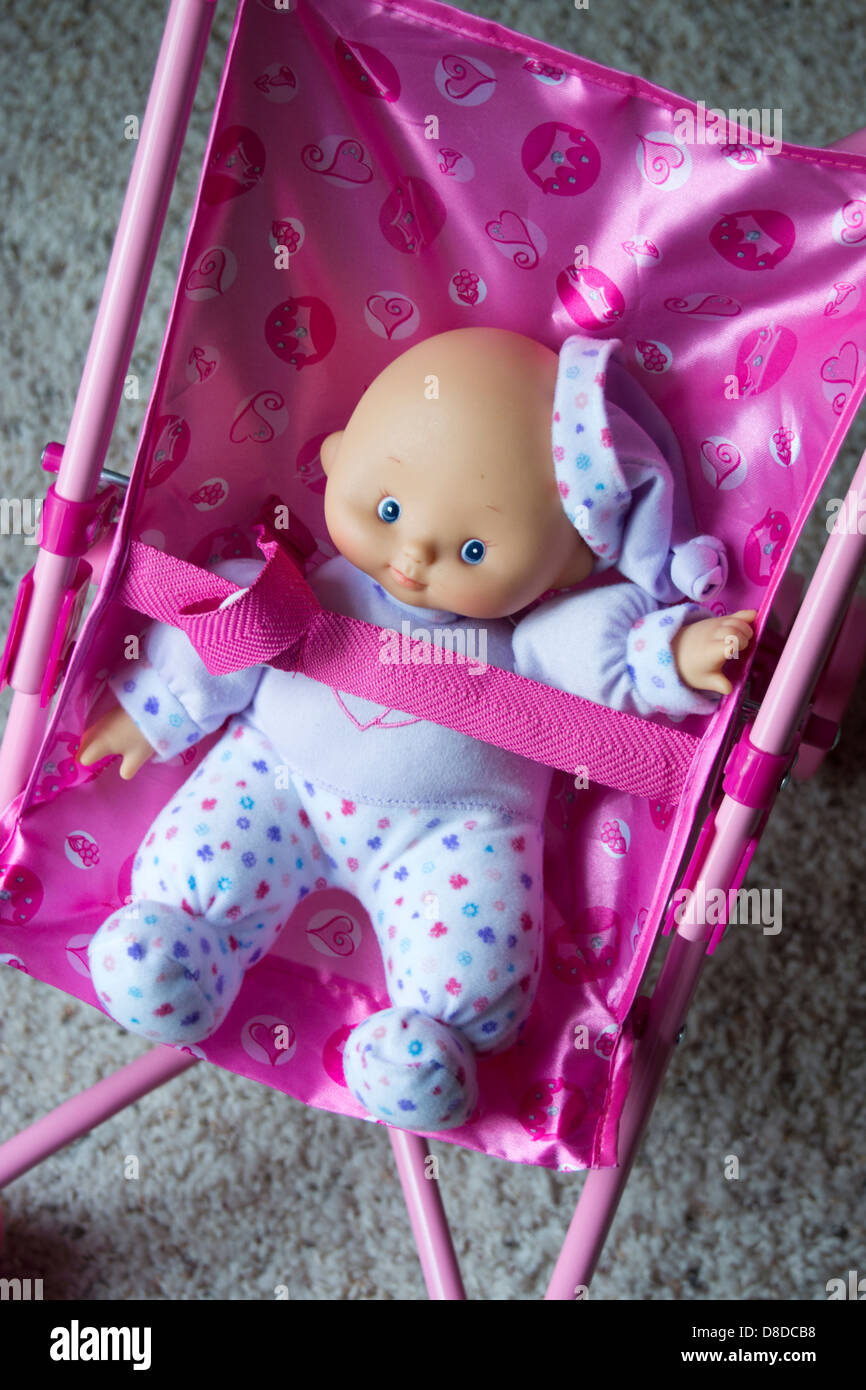 Child's doll safety belted into a toy stroller. Stock Photo