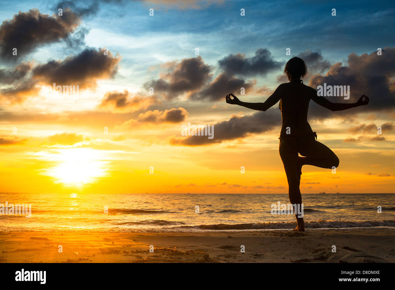 Girl practicing yoga by the sea at sunset. Stock Photo