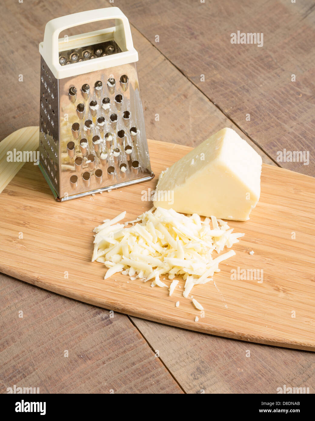 Parmesan Cheese and Grater Medium. an wider view of a block wedge of  parmesan cheese with shredded pieces all around and a metal cheese grater  on a cutting board Stock Photo