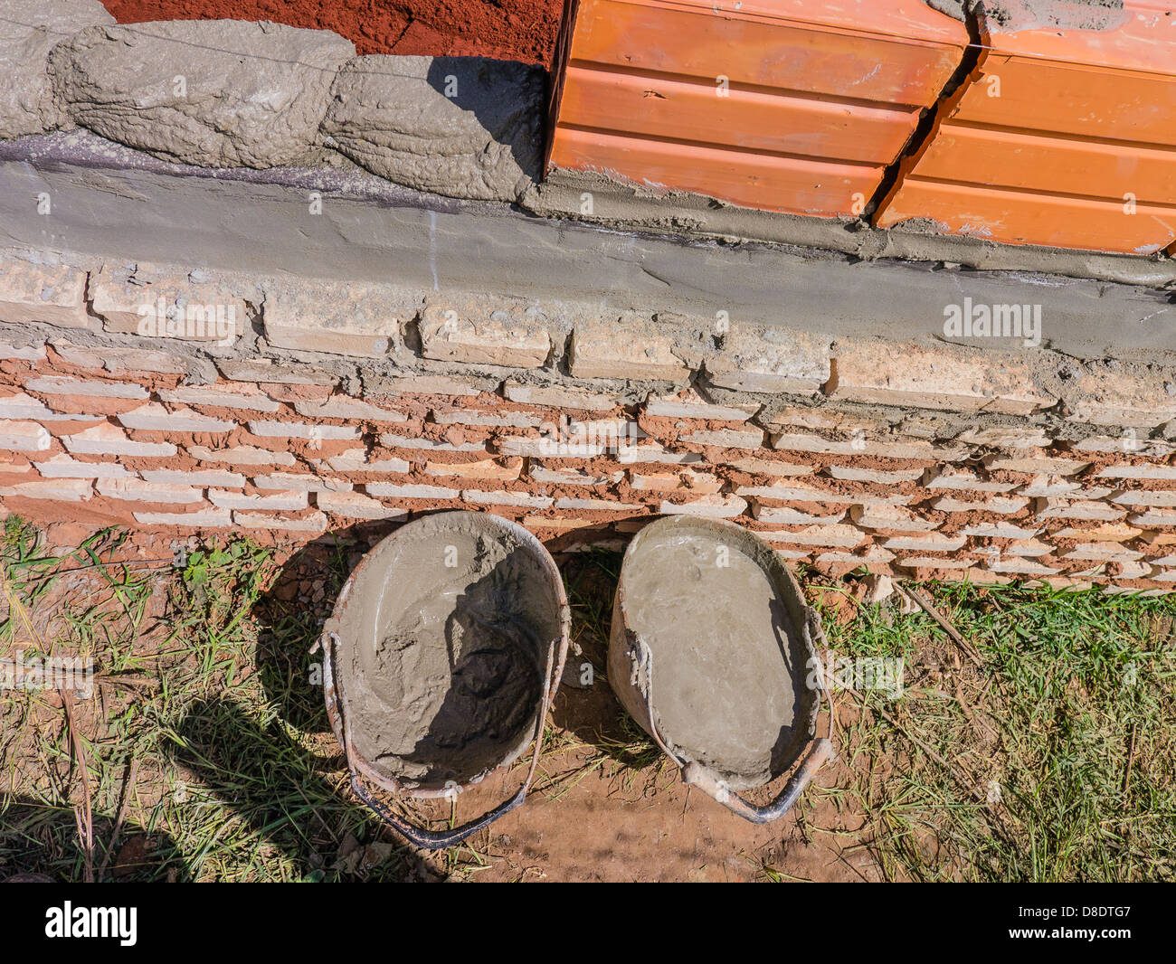 Two buckets of mortar sit by a newly laid course of bricks and ceramic blocks at a house construction site. Stock Photo