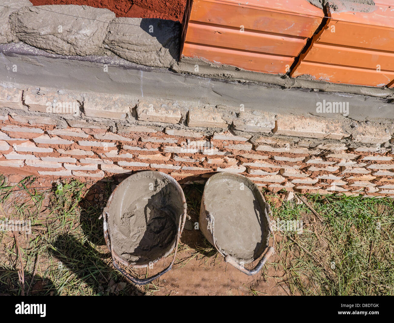 Two buckets of mortar sit by a newly laid course of bricks and ceramic blocks at a house construction site. Stock Photo