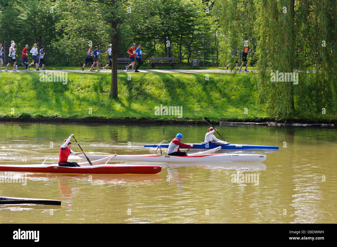 Male and female paddlers and canoeists rowing on the River Neckar, marathon runners in the background – Heilbronn Germany Stock Photo