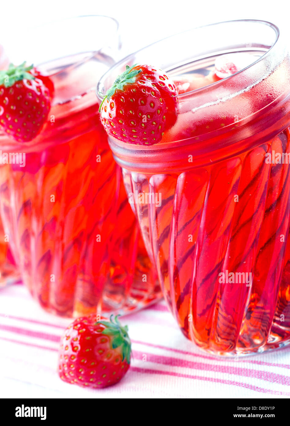 Glasses of red strawberry juice with frozen icecubes on vintage towel and wooden background Stock Photo