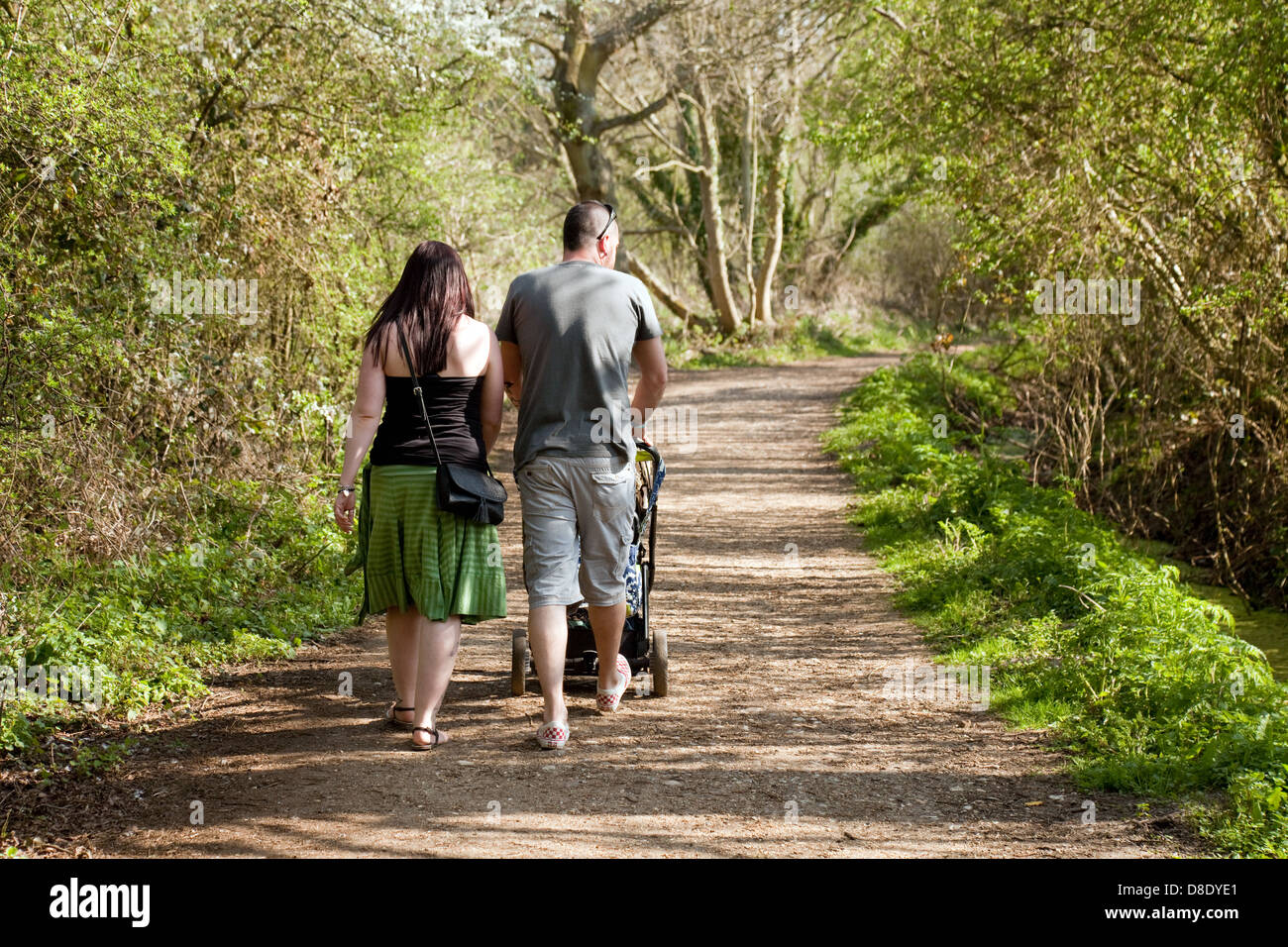A young couple family with a baby in a pushchair walking in the woods, Norfolk UK Stock Photo