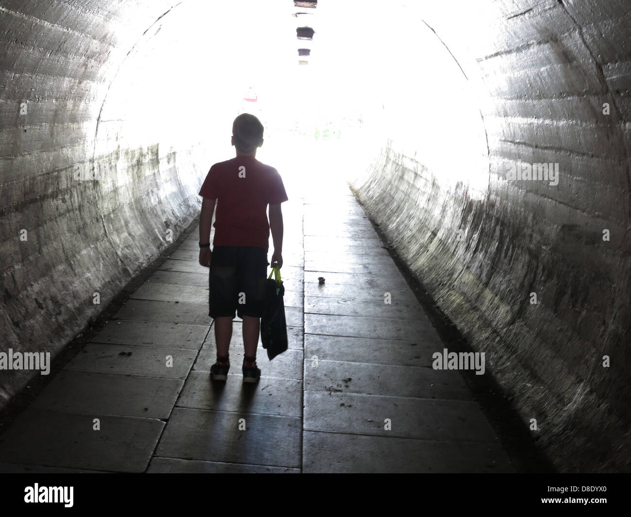 School age child walking home alone through a dark pedestrian subway, illustrating safeguarding concerns and dangers faced by children Stock Photo