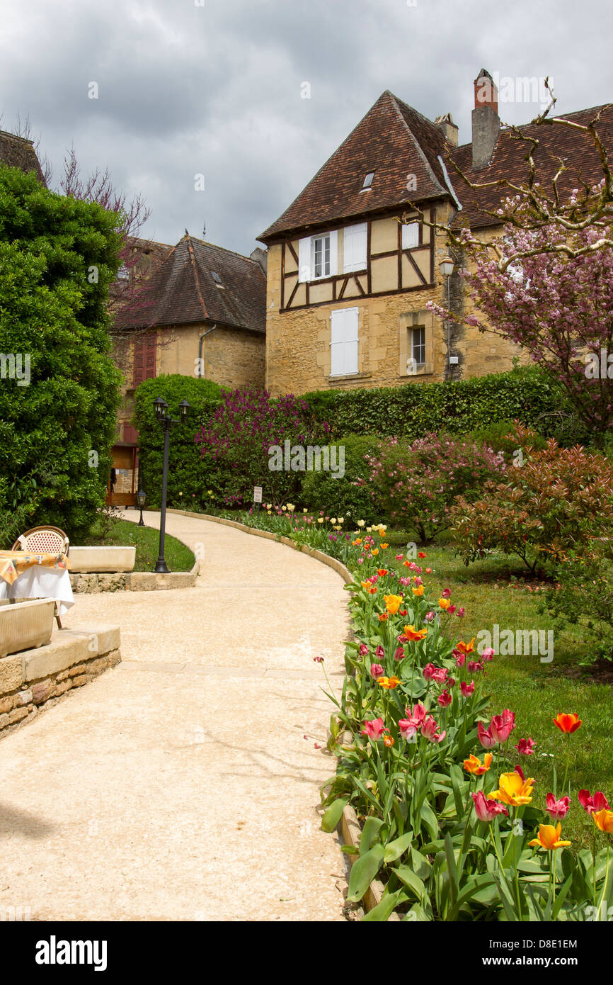 Tulips lining path from outdoor courtyard restaurant toward medieval sandstone buildings in Sarlat, Dordogne region of France Stock Photo