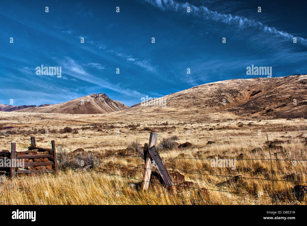 Barbed wire fence runs across dry field and hills on Squaw Butte near Emmett, Idaho Stock Photo