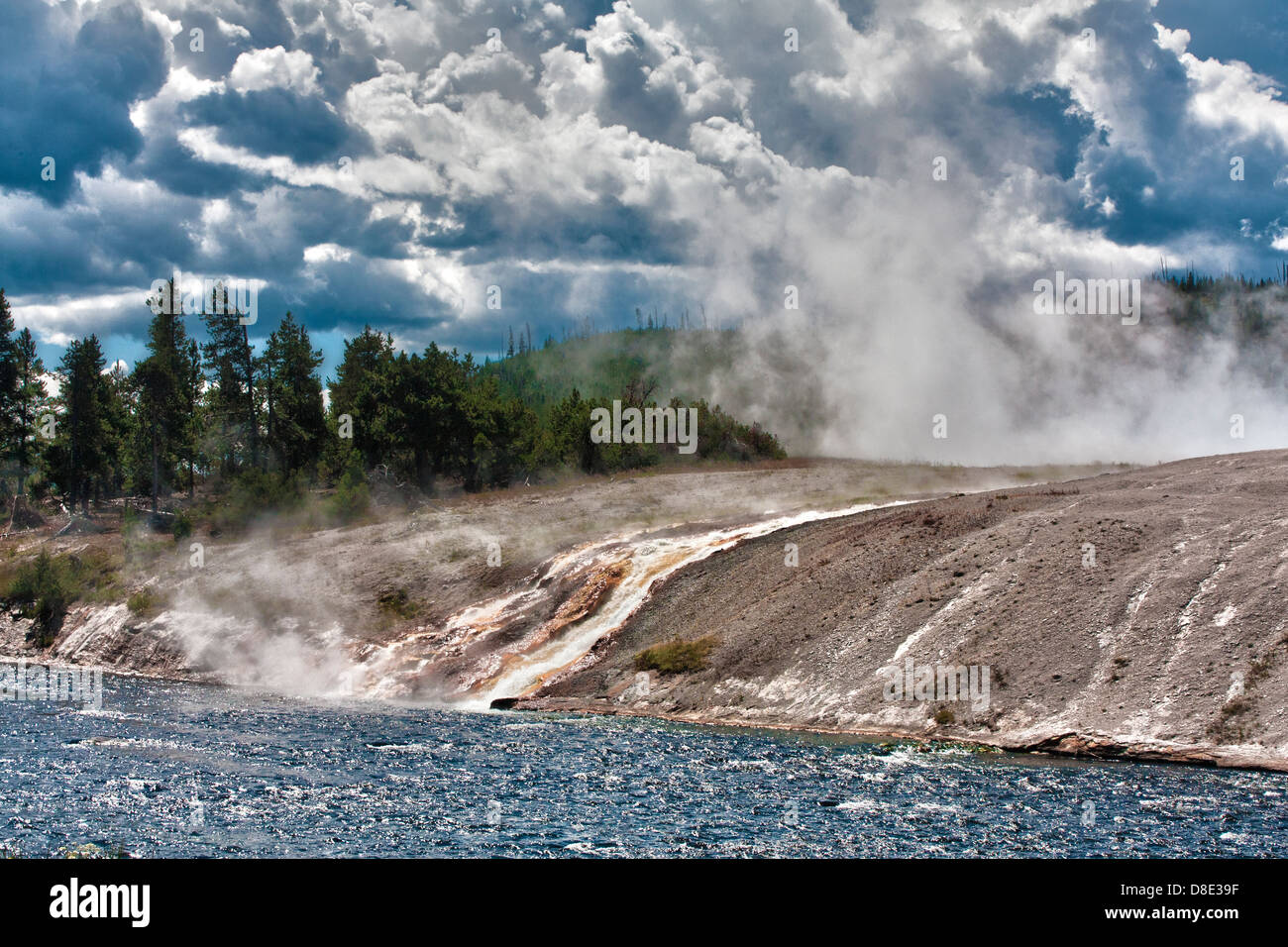 Steaming waterfalls overflow from Excelsior Geyser Crater into Firehole River in Midway Geyser Basin against stormy skies Stock Photo