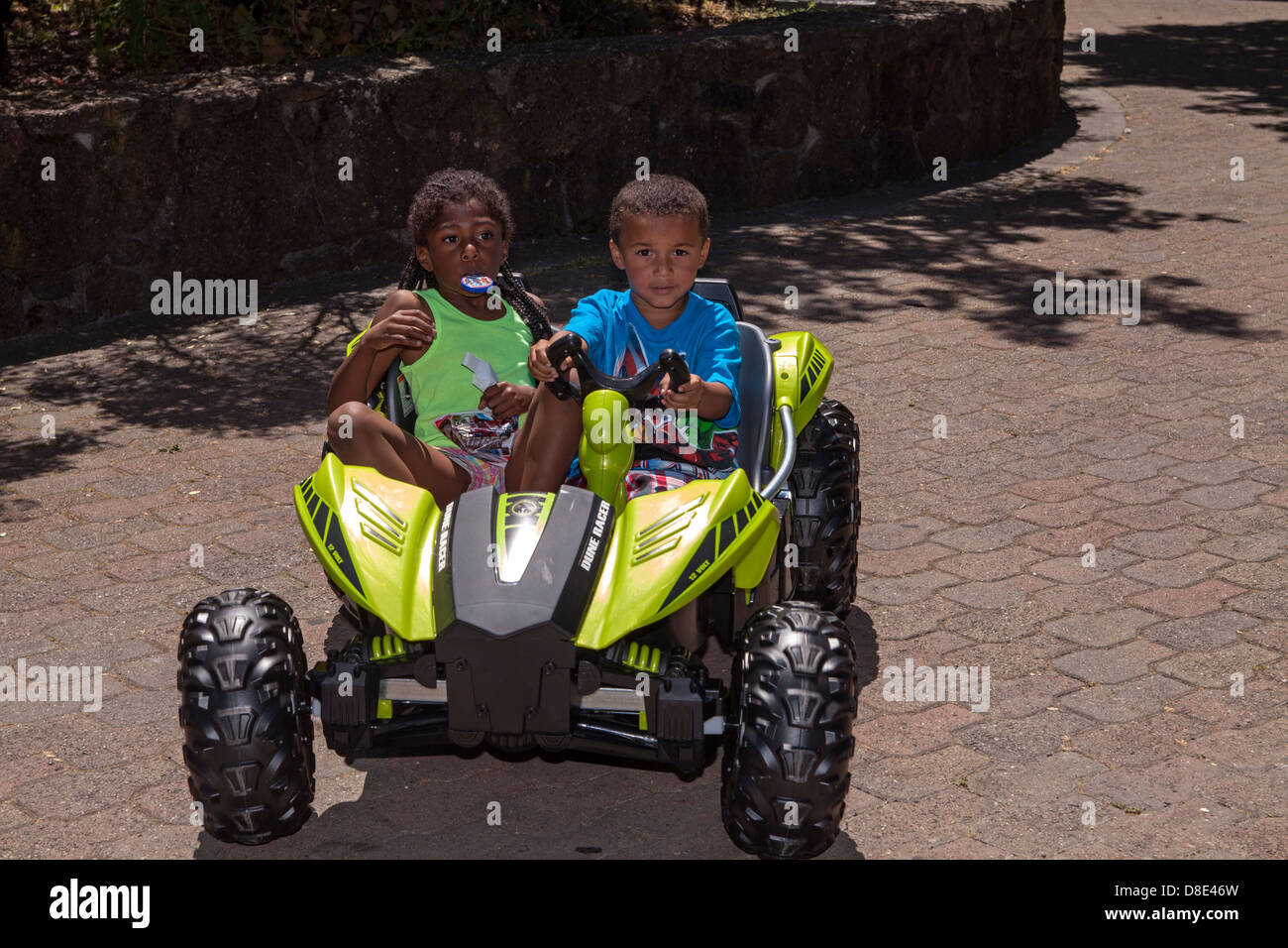 Little African American boy and girl riding an electrical go-cart, Finley Park, Santa Rosa, California, USA, North America Stock Photo