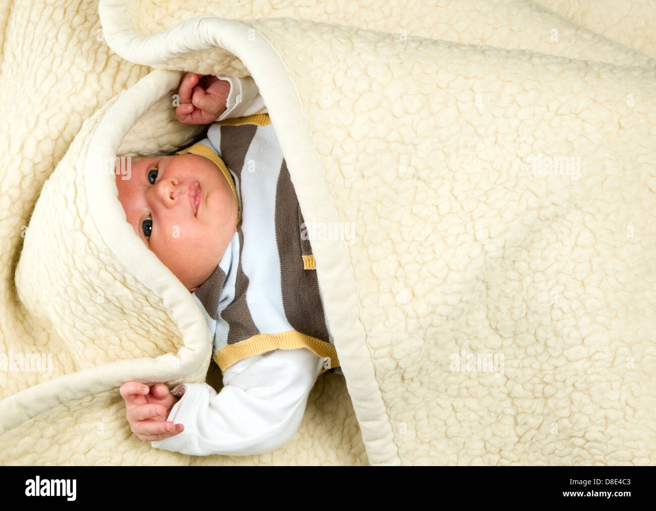 Beautiful white baby boy with big eyes is lying under blanket Stock Photo