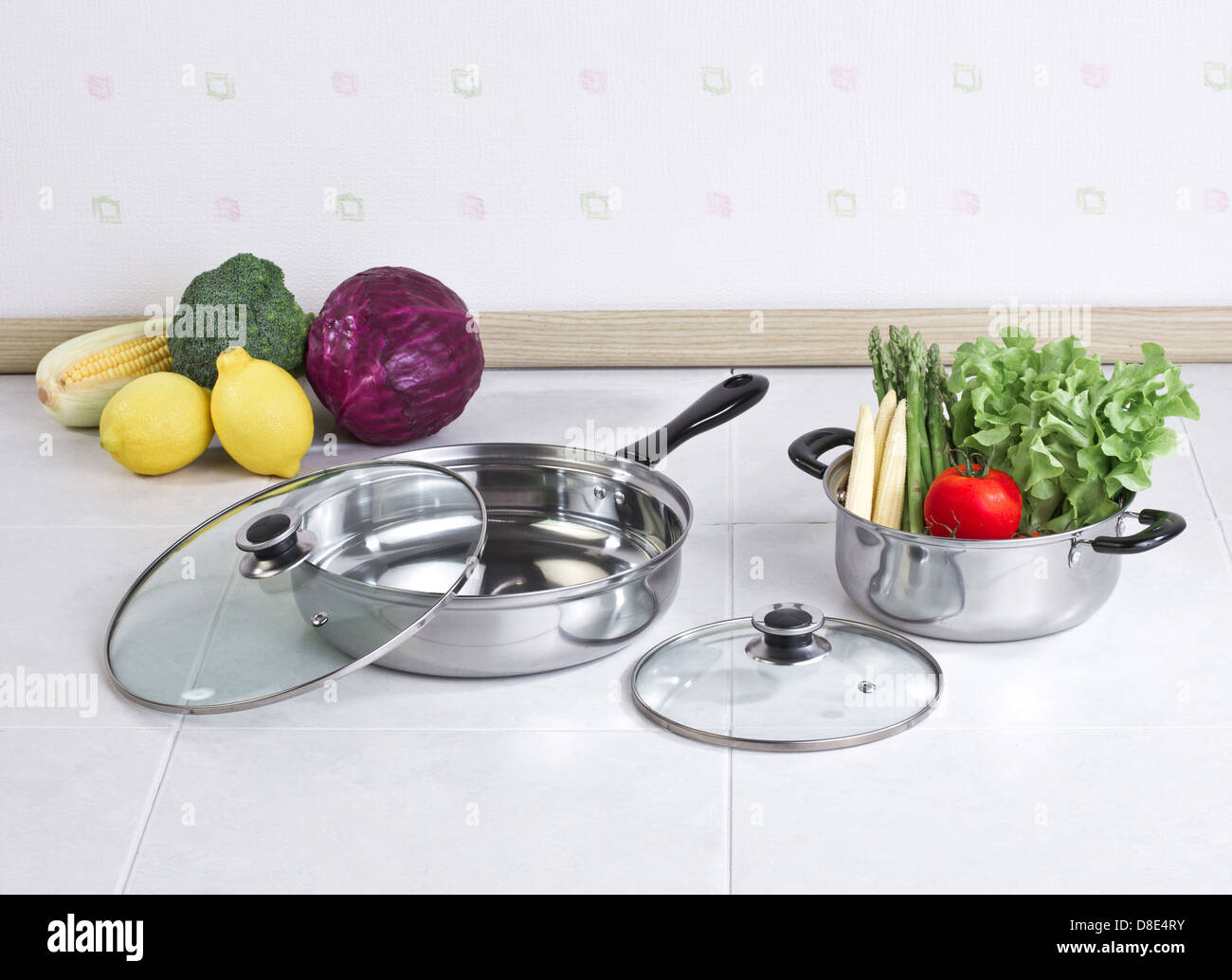 Set of stainless pot and pan with glass lids and vegetables Stock Photo