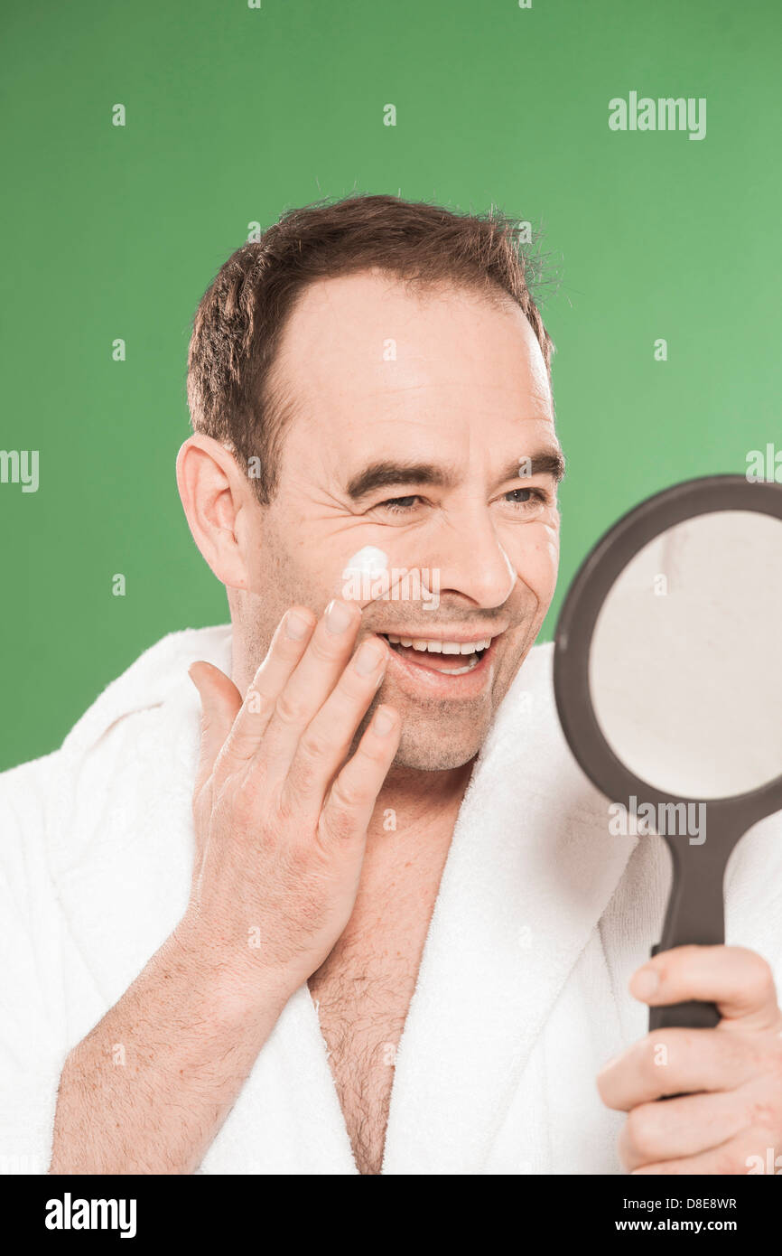 Happy man in bathrobe applying facial cream Stock Photo