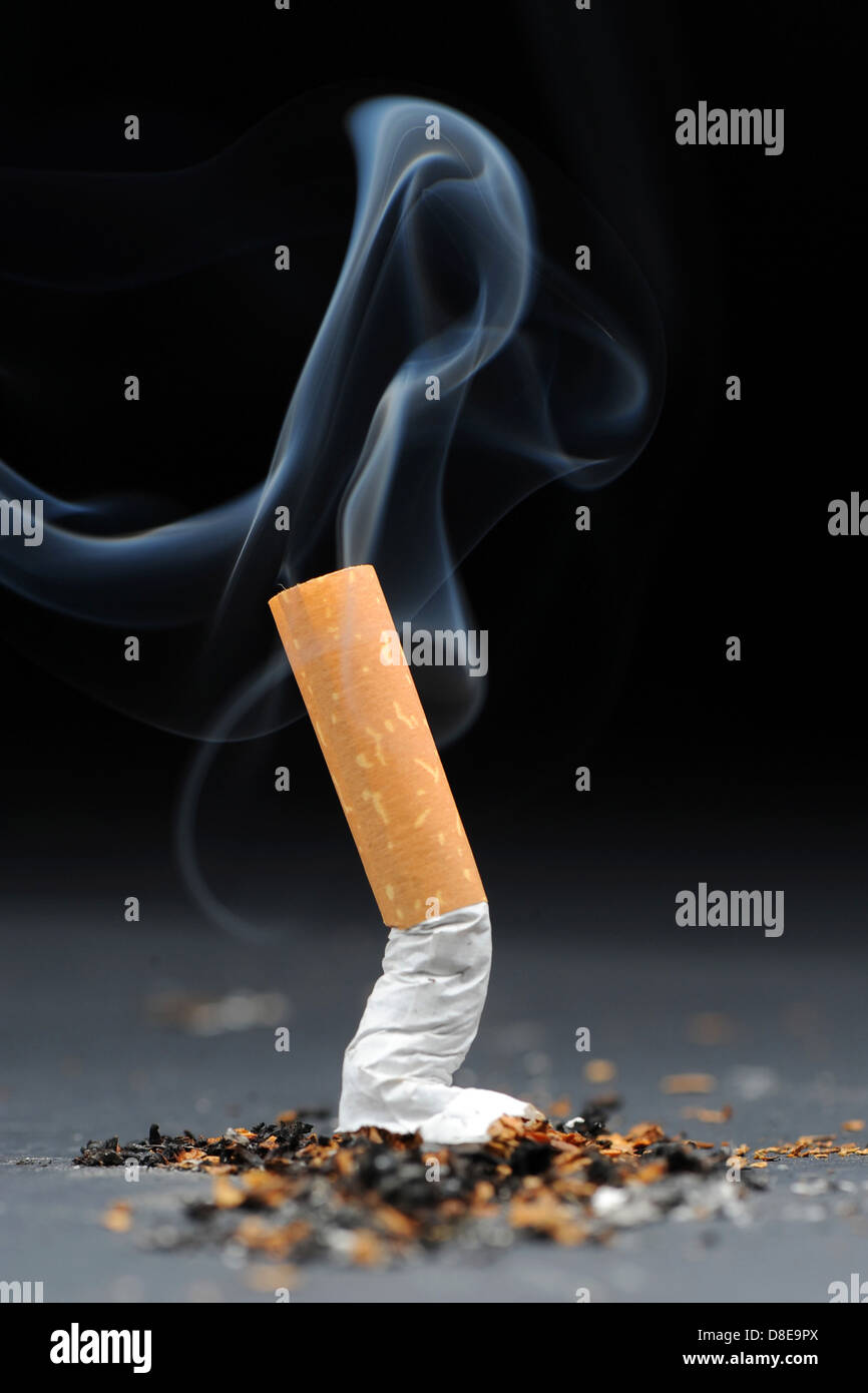 A burning cigarette with smoke against a black background. Stock Photo