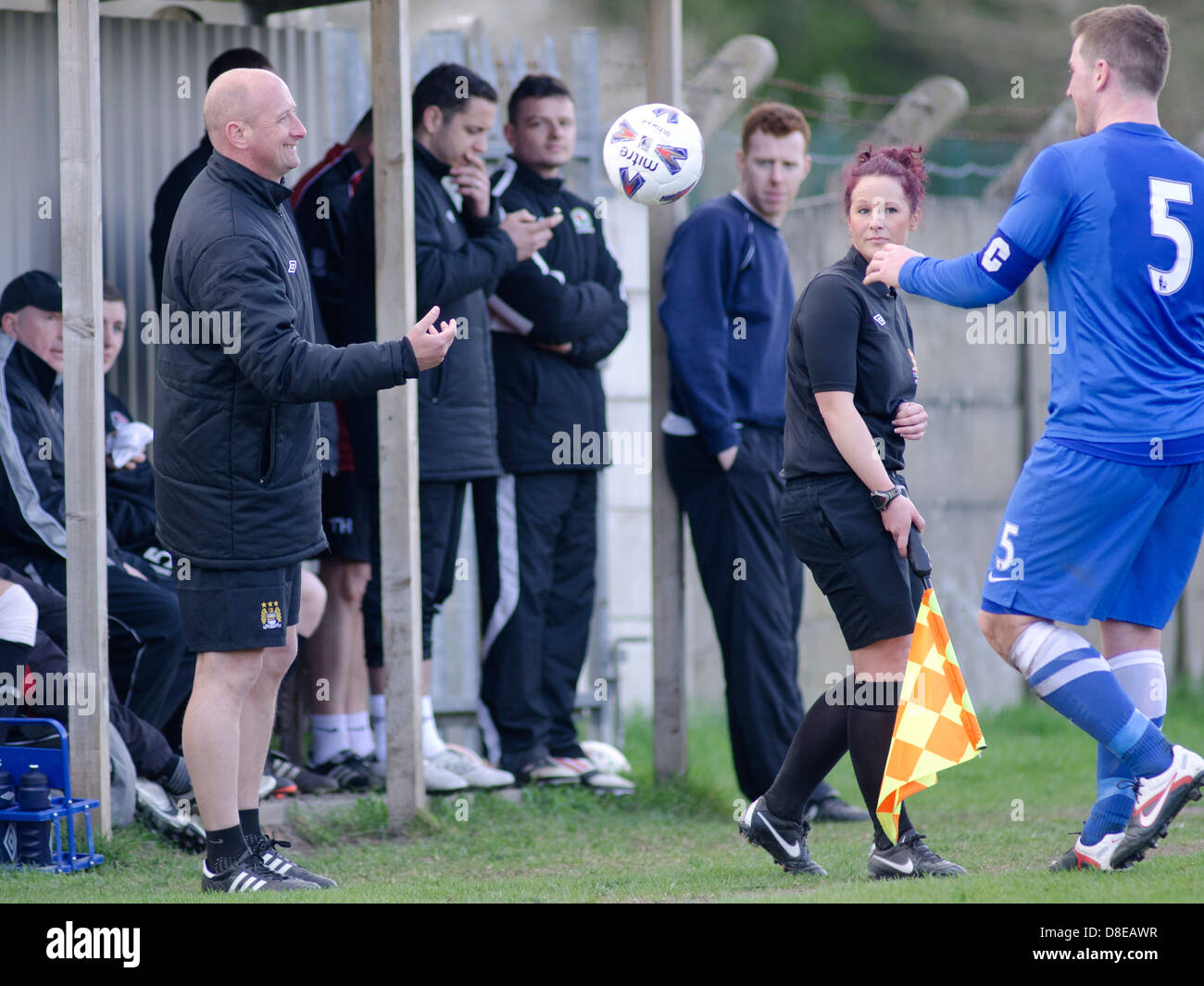 A football coach throws the ball back to an opposition player while a female linesman watches Stock Photo