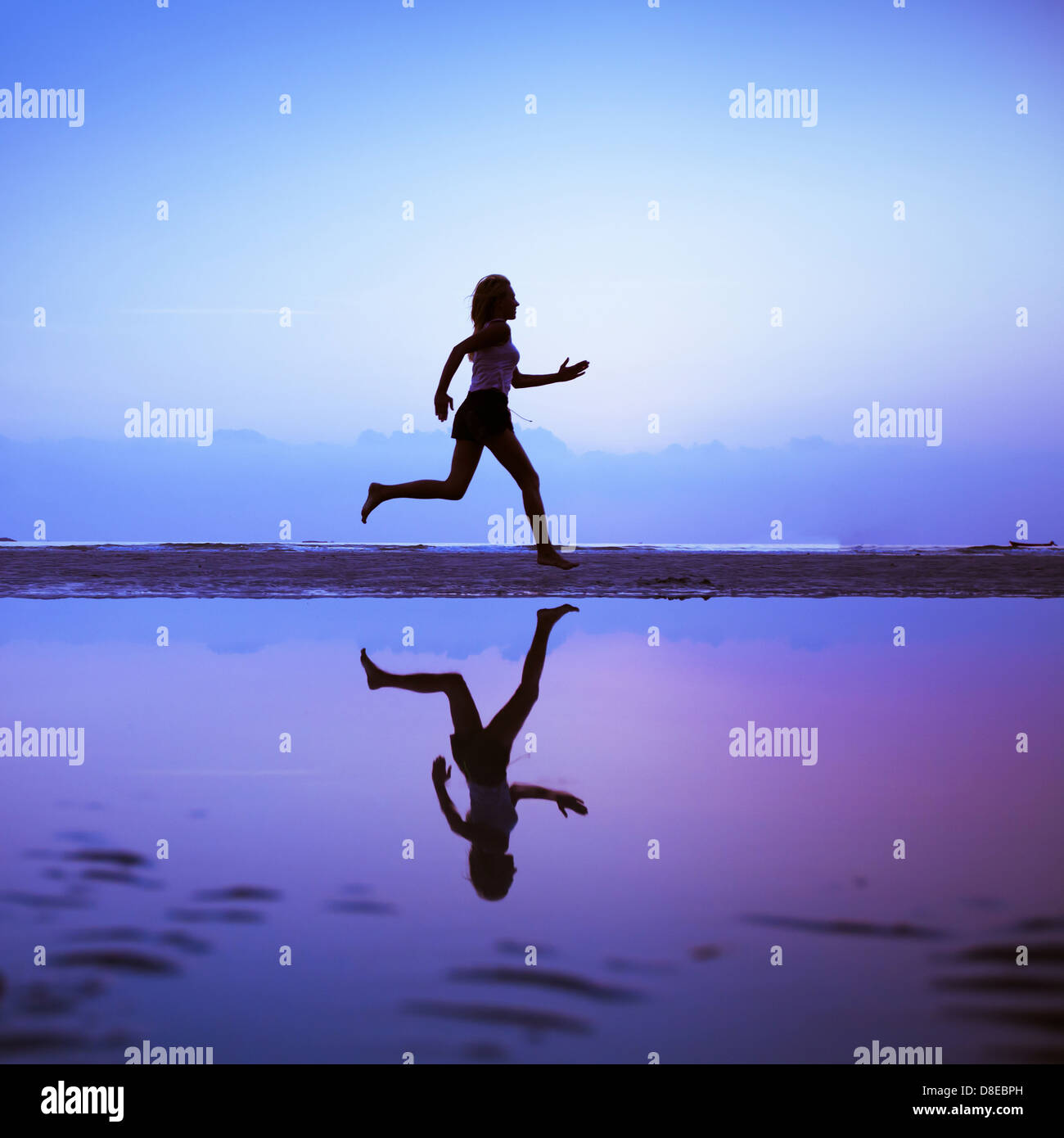 Female runner silhouette is mirrored below with a blue sunset sky as background Stock Photo