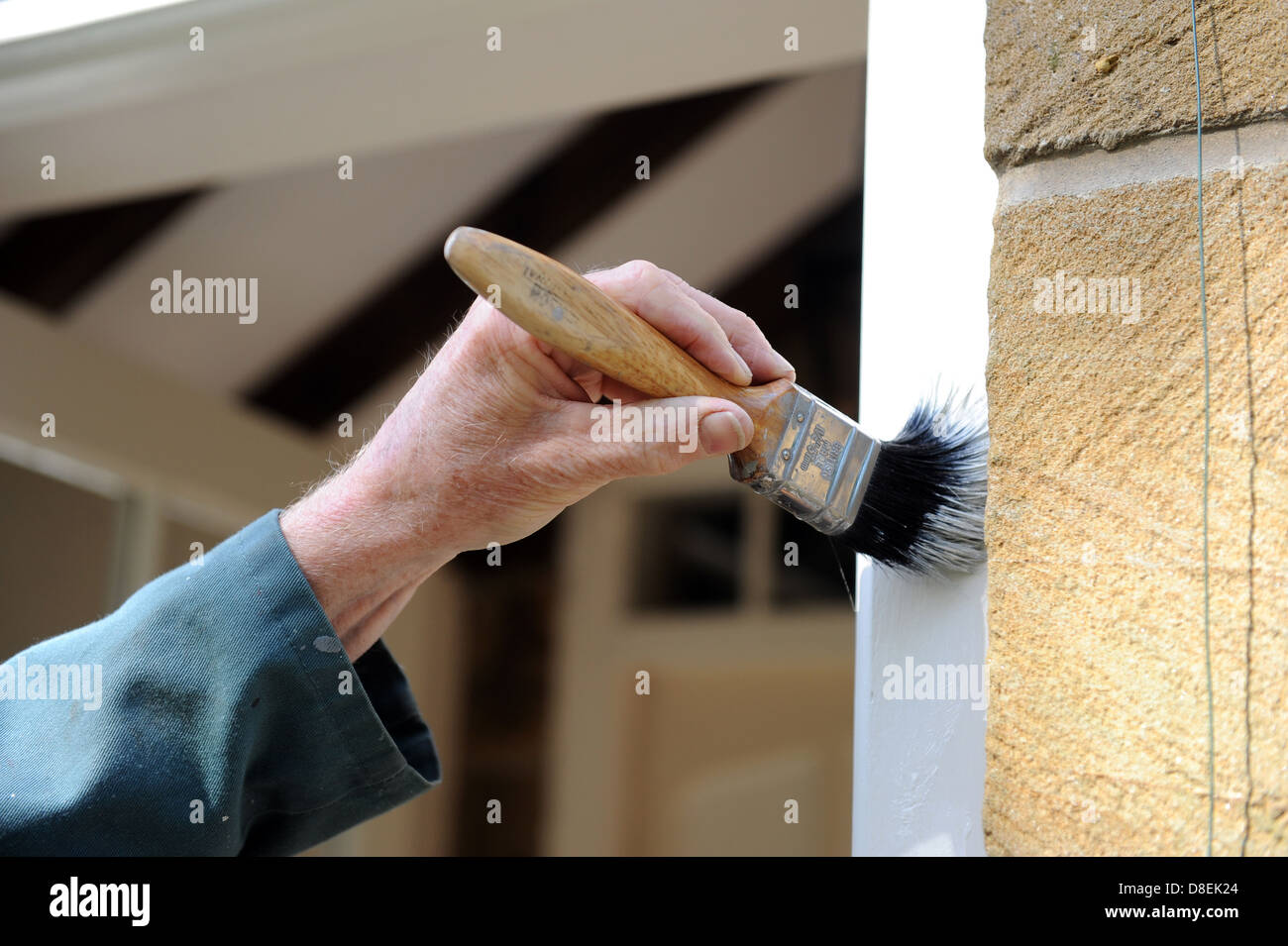 Elderly male painting the door frame on the porch of his house Stock