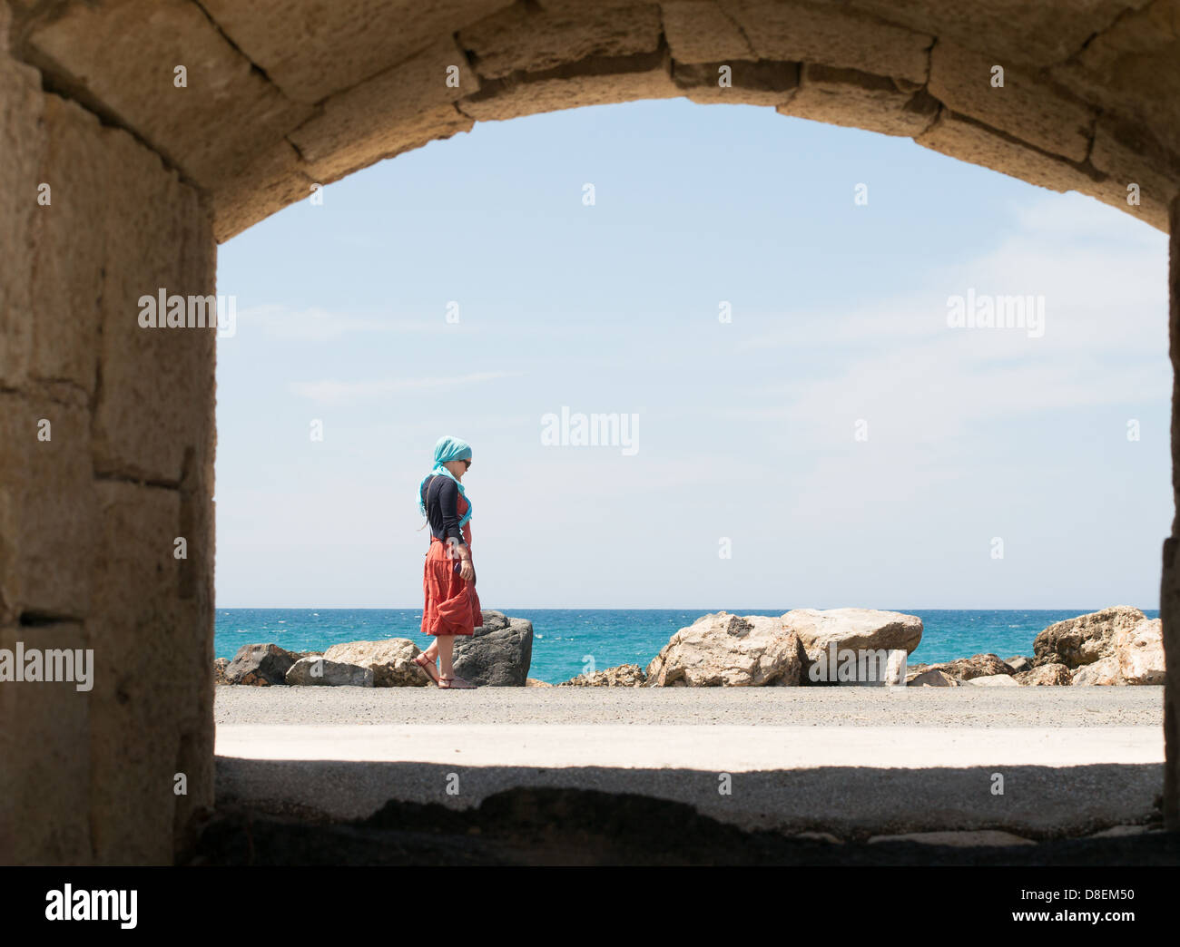 Woman, framed by arch, walking along the pier at Heraklion, Crete, Greece Stock Photo