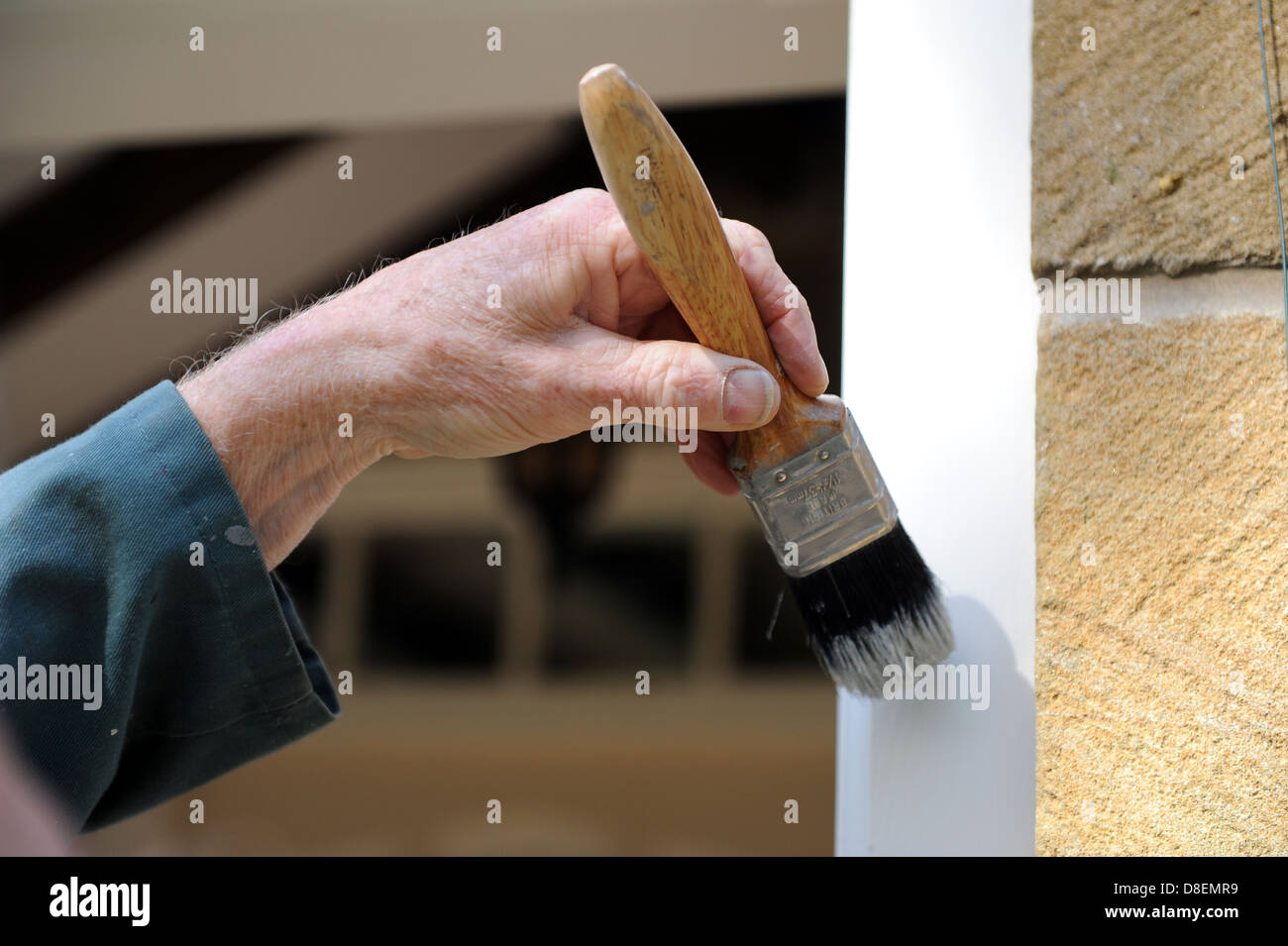 Elderly male painting the door frame on the porch of his house Stock