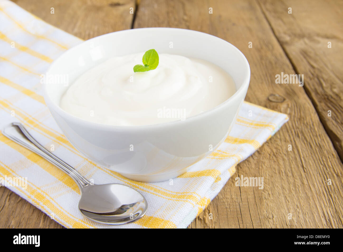 Fresh white plain yogurt in bowl with mint and spoon over rustic wooden background (table) close up, copy space Stock Photo