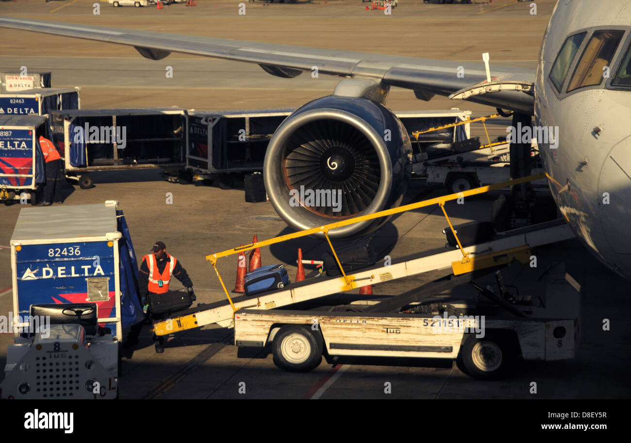 A baggage handler for Delta Airlines places baggage onto a conveyer belt in preperation for a flight. Stock Photo