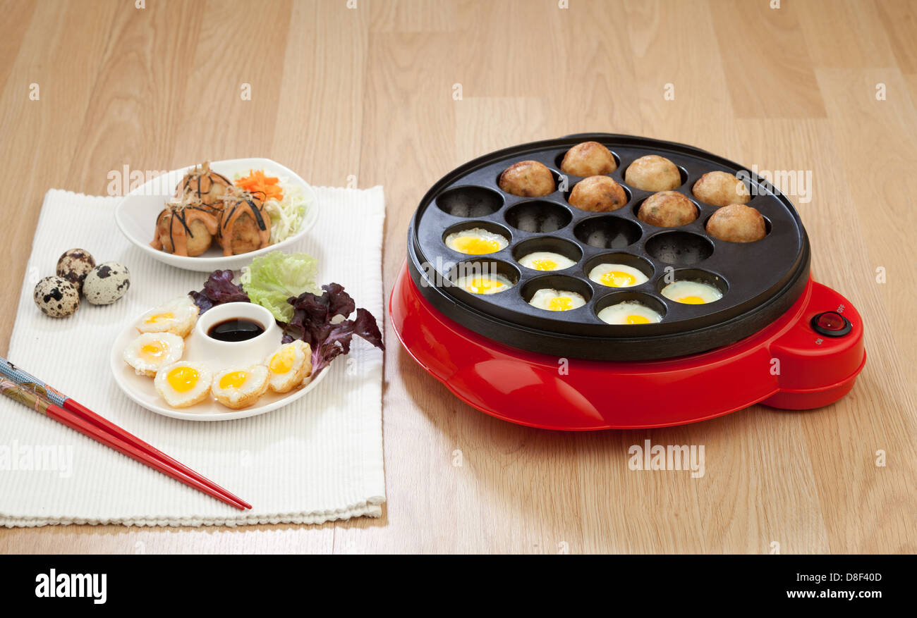 Takoyaki ball cooking machine display with takoyaki and fried eggs on wooden background Stock Photo