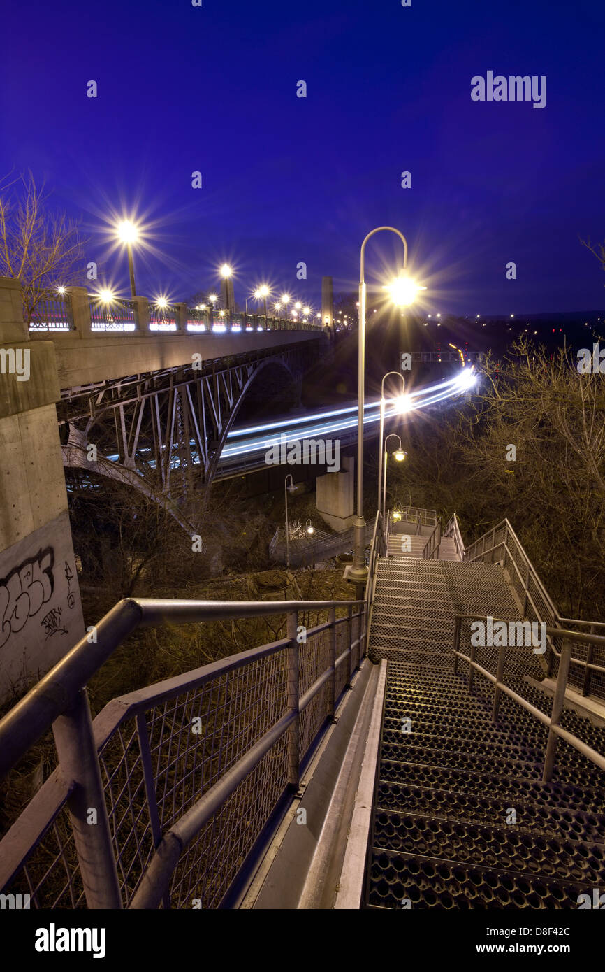 A steel stairwell leading down under a bridge with a train passing by in Hamilton, Ontario. Stock Photo