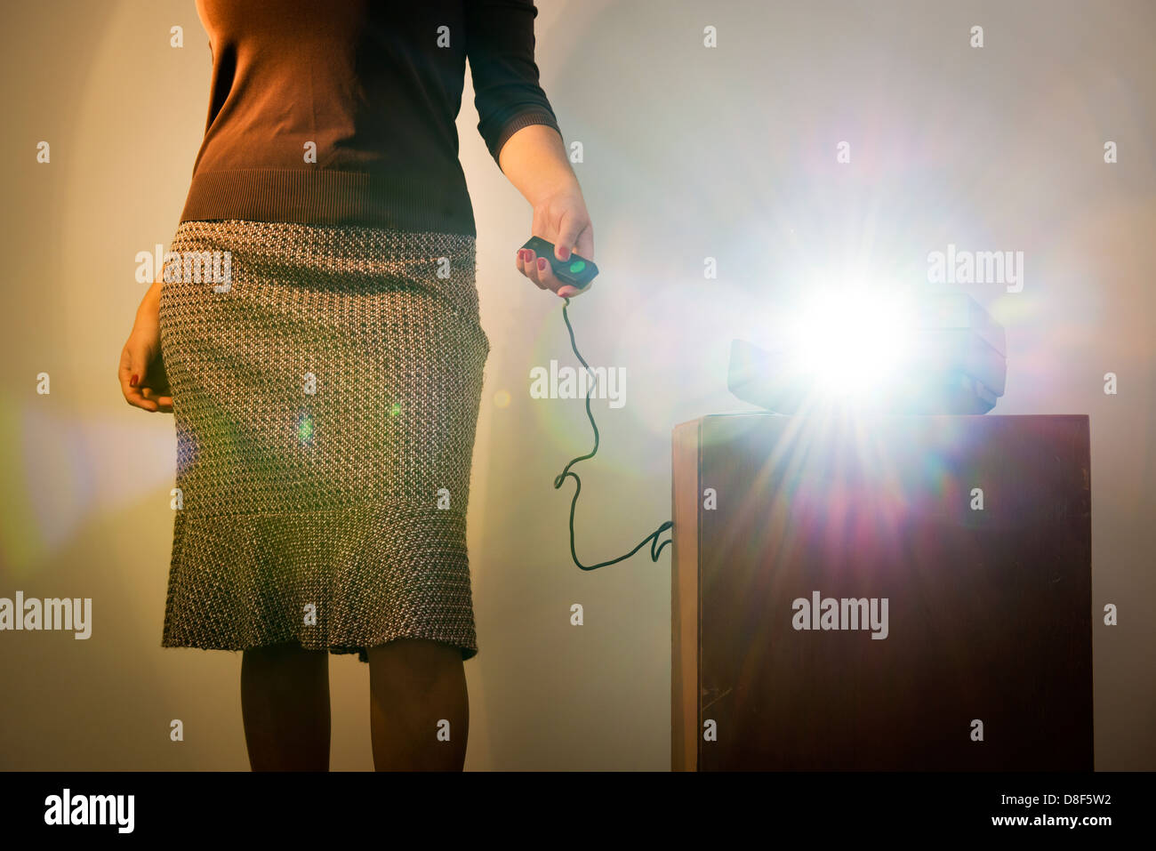 Retro styled woman operating a slide projector with a wired remote control and lens flare from projector light Stock Photo