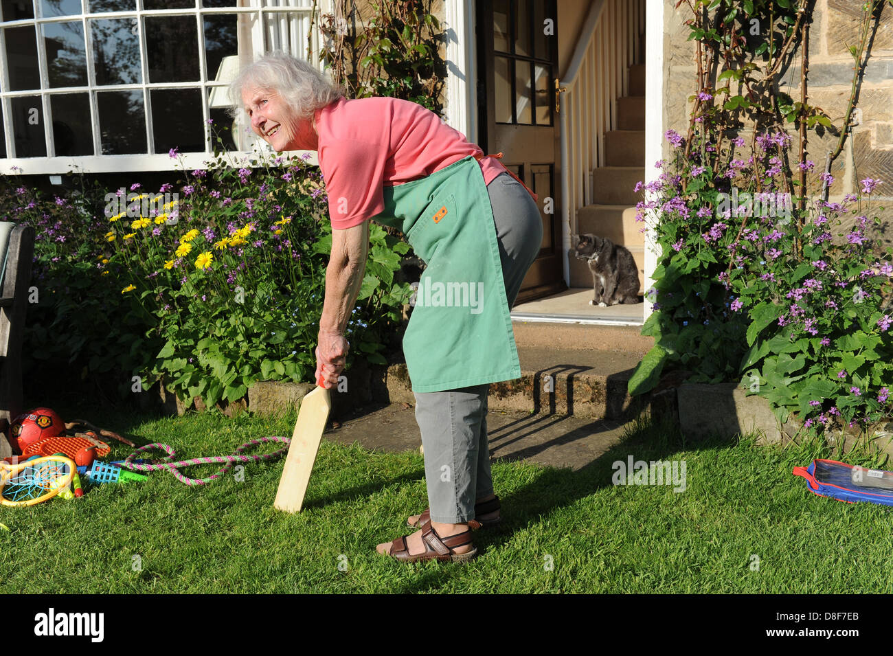 Elderly grandmother playing a game of cricket in the garden of her family home in North Yorkshire. Stock Photo