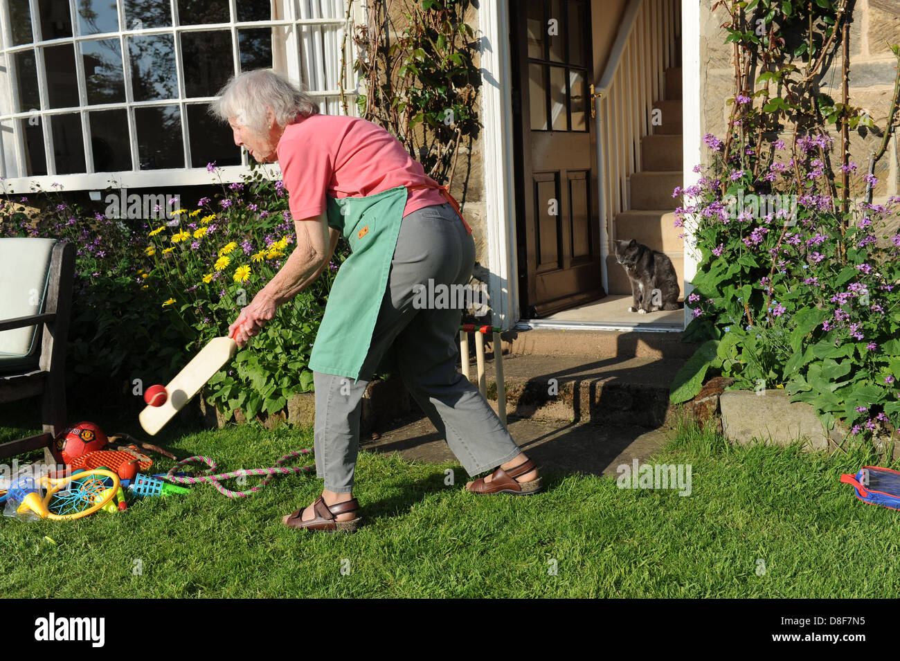 Elderly grandmother playing a game of cricket in the garden of her family home in North Yorkshire. Stock Photo
