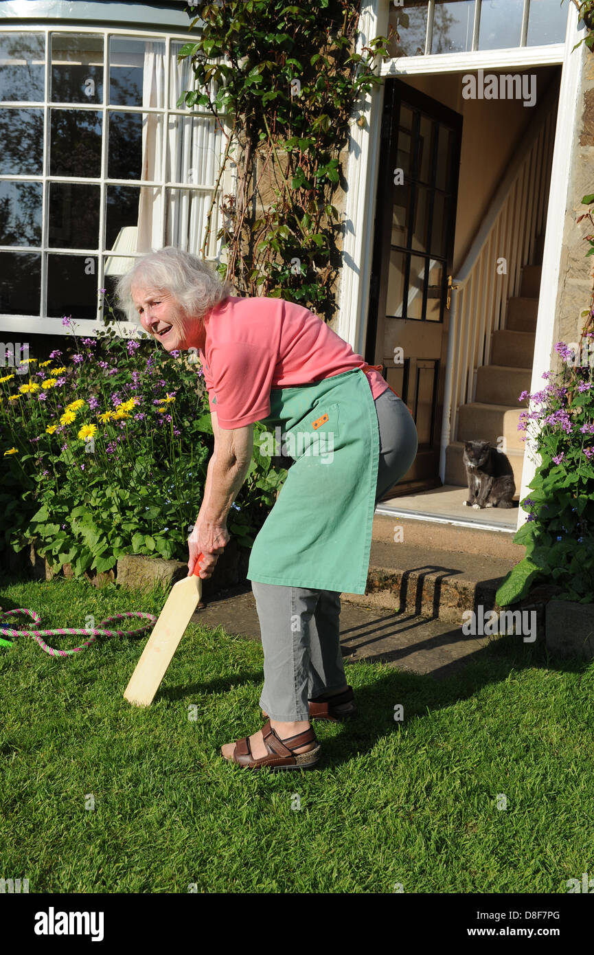 Elderly grandmother playing a game of cricket in the garden of her family home in North Yorkshire. Stock Photo