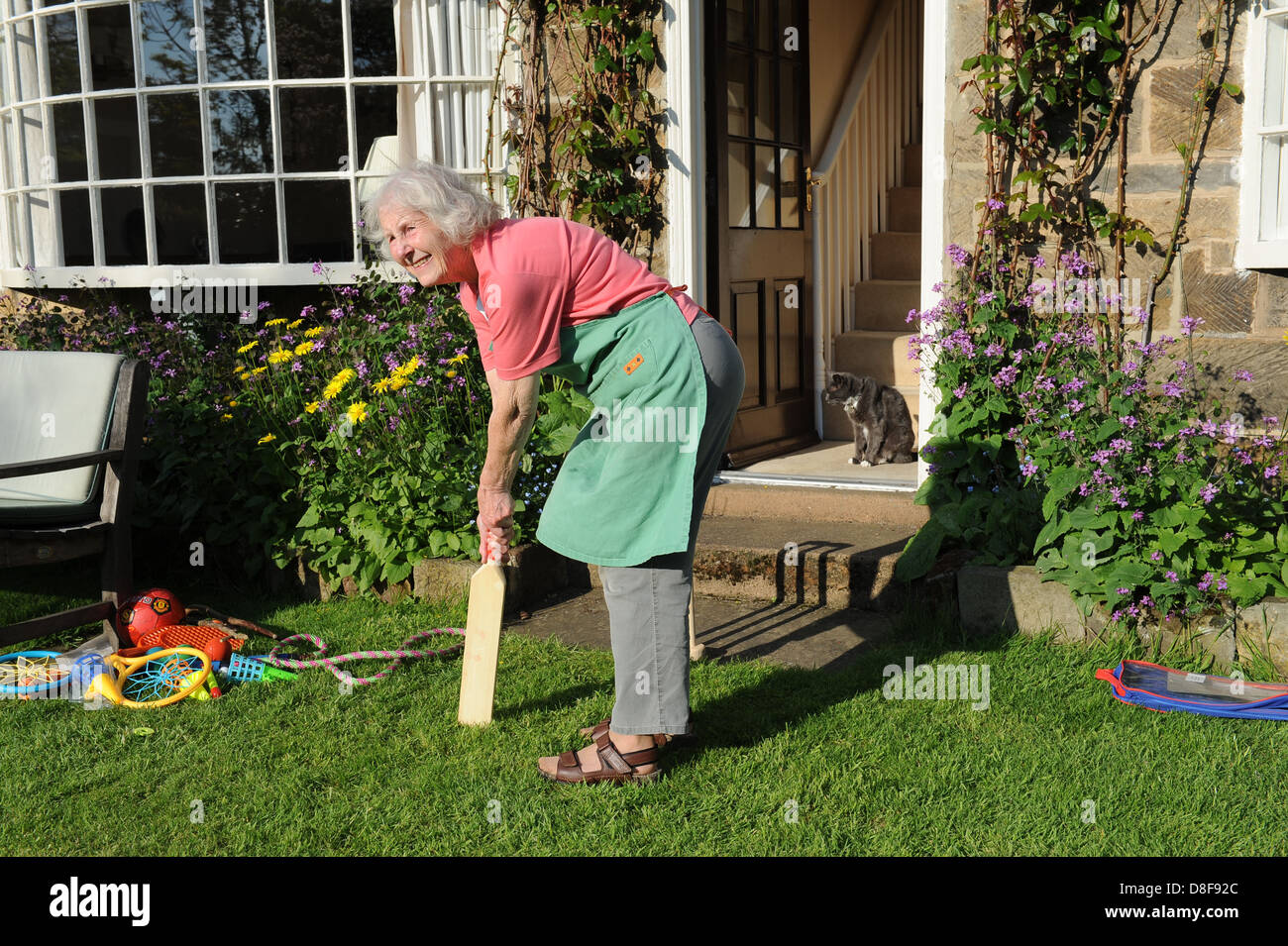 Elderly grandmother playing a game of cricket in the garden of her family home in North Yorkshire. Stock Photo
