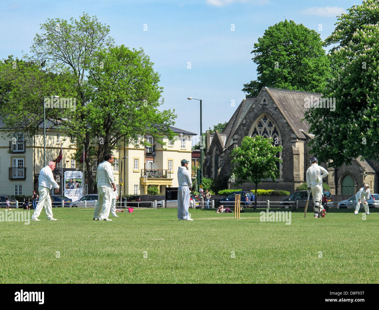 Cricketers playing cricket under a blue sky on Twickenham Green in Summer Stock Photo