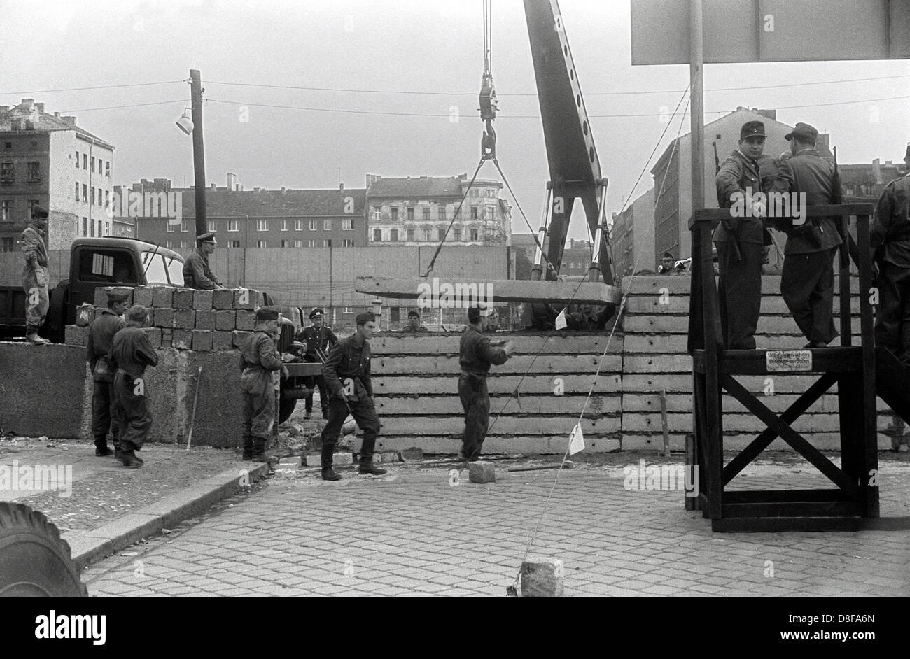 Wenige Tage nach dem 13.August 1961 errichten Ostberliner Bauarbeiter unter der Aufsicht von bewaffneten Volkspolizisten eine Mauer an der Bernauer Straße im Westberliner Bezirk Wedding. Die Bernauerstraße grenzte den französischen von dem sowjetischen Sektor ab. Bereits am Morgen des 13.August hatten DDR-Streitkräfte damit begonnen, den Ostteil der Stadt mit Straßensperren aus Stacheldraht in Richtung Westen zu sperren. Die Mauer sollte den ständig steigenden Strom von Flüchtlingen nach Westberlin aufhalten. Foto: von Keussler Stock Photo