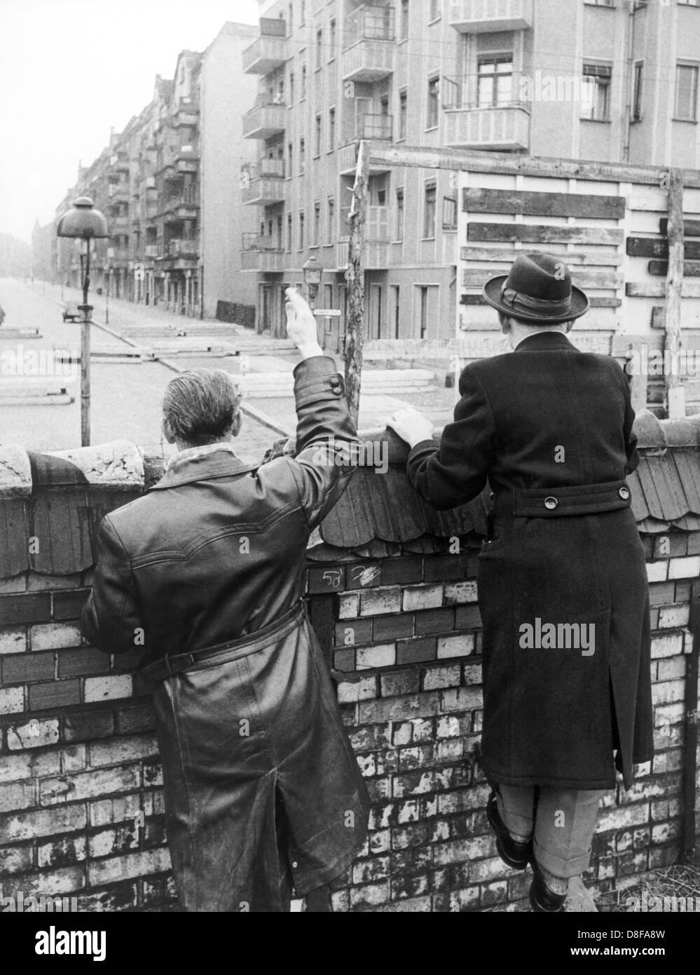 Westberliner Männer winken, solange die Möglichkeit noch besteht, im Jahr 1962 ihren Verwandten und Bekannten in Ostberlin zu. Volkspolizisten der DDR sind damit beschäftigt, eine Sichtblende zu errichten. Am frühen Sonntagmorgen des 13. August 1961 wurde unter der Aufsicht von bewaffneten Streitkräften der DDR mit der Errichtung von Straßensperren aus Stacheldraht und dem Bau einer Mauer begonnen, um den Ostteil Berlins vom Westteil abzusperren. Die Mauer sollte den ständig steigenden Flüchtlingsstrom von Ost- nach West-Berlin stoppen. +++(c) dpa - Report+++ Stock Photo