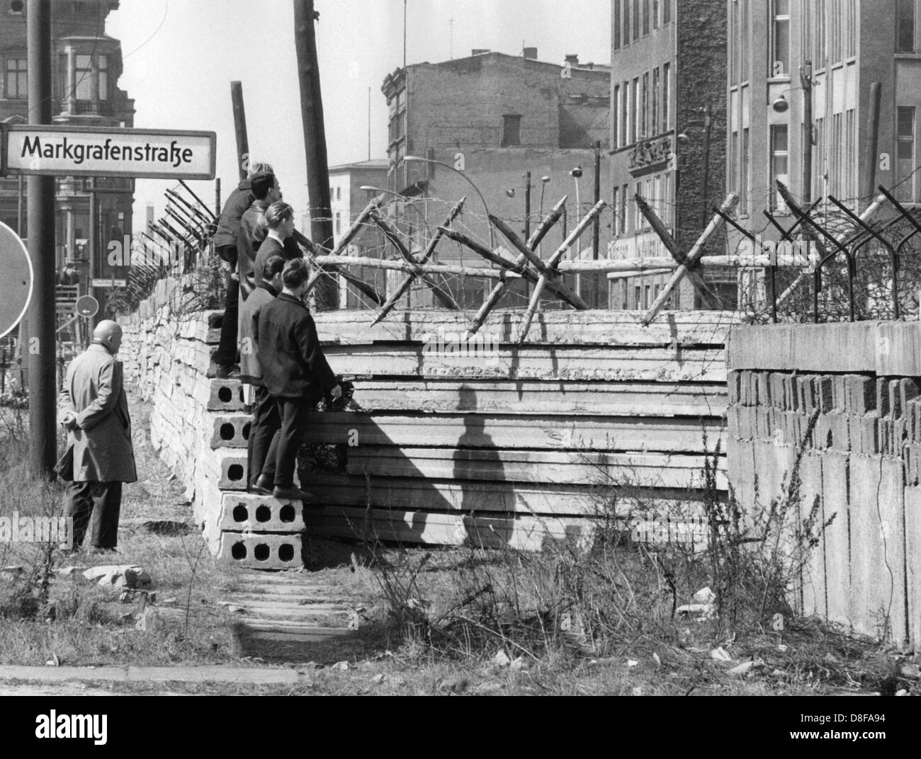 Westberliner Männer werfen am 17.04.1964 einen Blick über die im Bau befindliche vorverlegte Mauer an der Markgrafenstraße in Berlin. Am frühen Sonntagmorgen des 13. August 1961 wurde unter der Aufsicht von bewaffneten Streitkräften der DDR mit der Errichtung von Straßensperren aus Stacheldraht und dem Bau einer Mauer begonnen, um den Ostteil Berlins vom Westteil abzusperren. Die Mauer sollte den ständig steigenden Flüchtlingsstrom von Ost- nach West-Berlin stoppen. +++(c) dpa - Report+++ Stock Photo