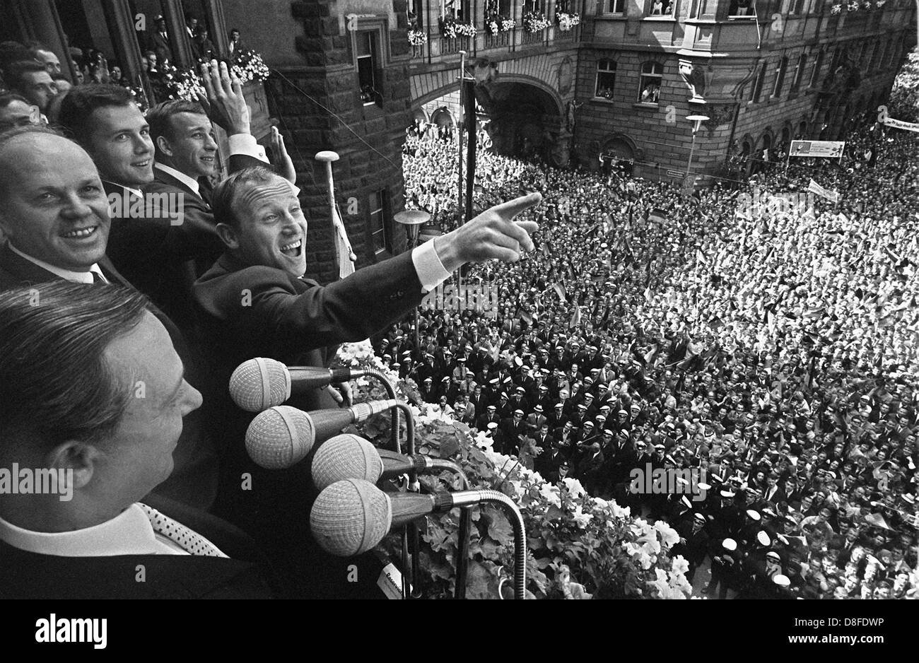 An enthusiastic crowd of people at the Frankfurt Roemerberg are celebrating the German players who are standing on the balcony of the townhall on July 31st 1966. In the front Frankfurt's Mayor Willi Brundert, in the middle with pointing index finger Uwe Seeler and behind him Franz Beckenbauer. Host country England had won the 1966 FIFA World Cup final 4:2 after extra time against Germany. Stock Photo