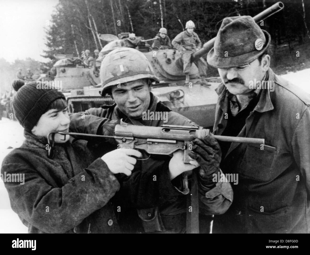 A soldier of the US army (centre), which was in Germany for the participation in the manoeuvre REFORGER I, shows to the twelve-year-old Franzl (left) and his father (right) how to handle a new submachine gun. Altogether around 17.000 soldiers participated in the manoeuvre, many of them were brought from the USA to Germany via air bridge. Stock Photo