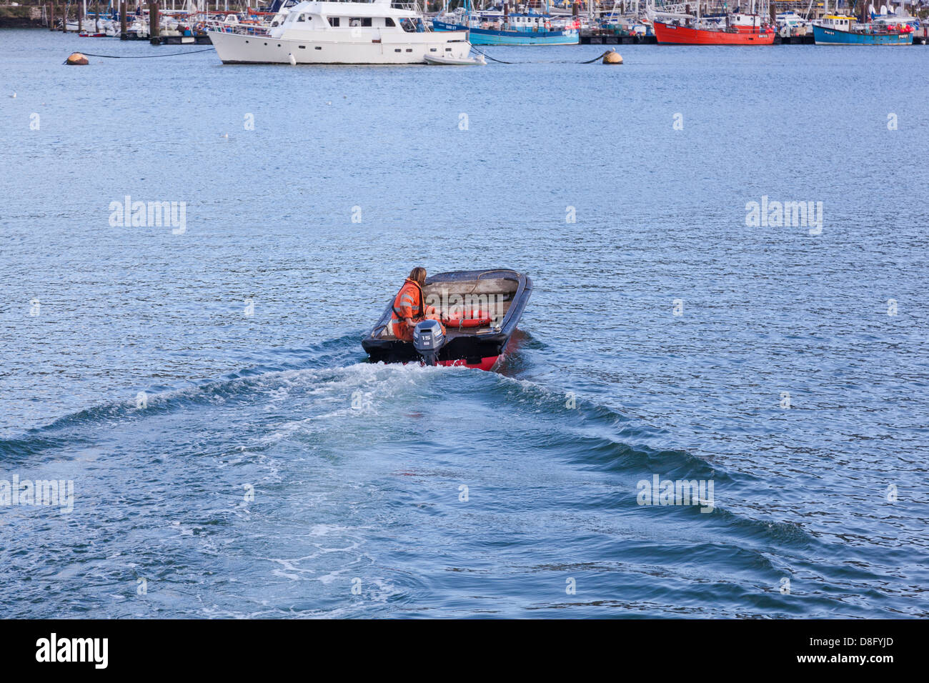 Man dressed in hi-viz orange jacket sails across the River Dart in Dartmouth in a small dinghy with an outboard motor. Stock Photo