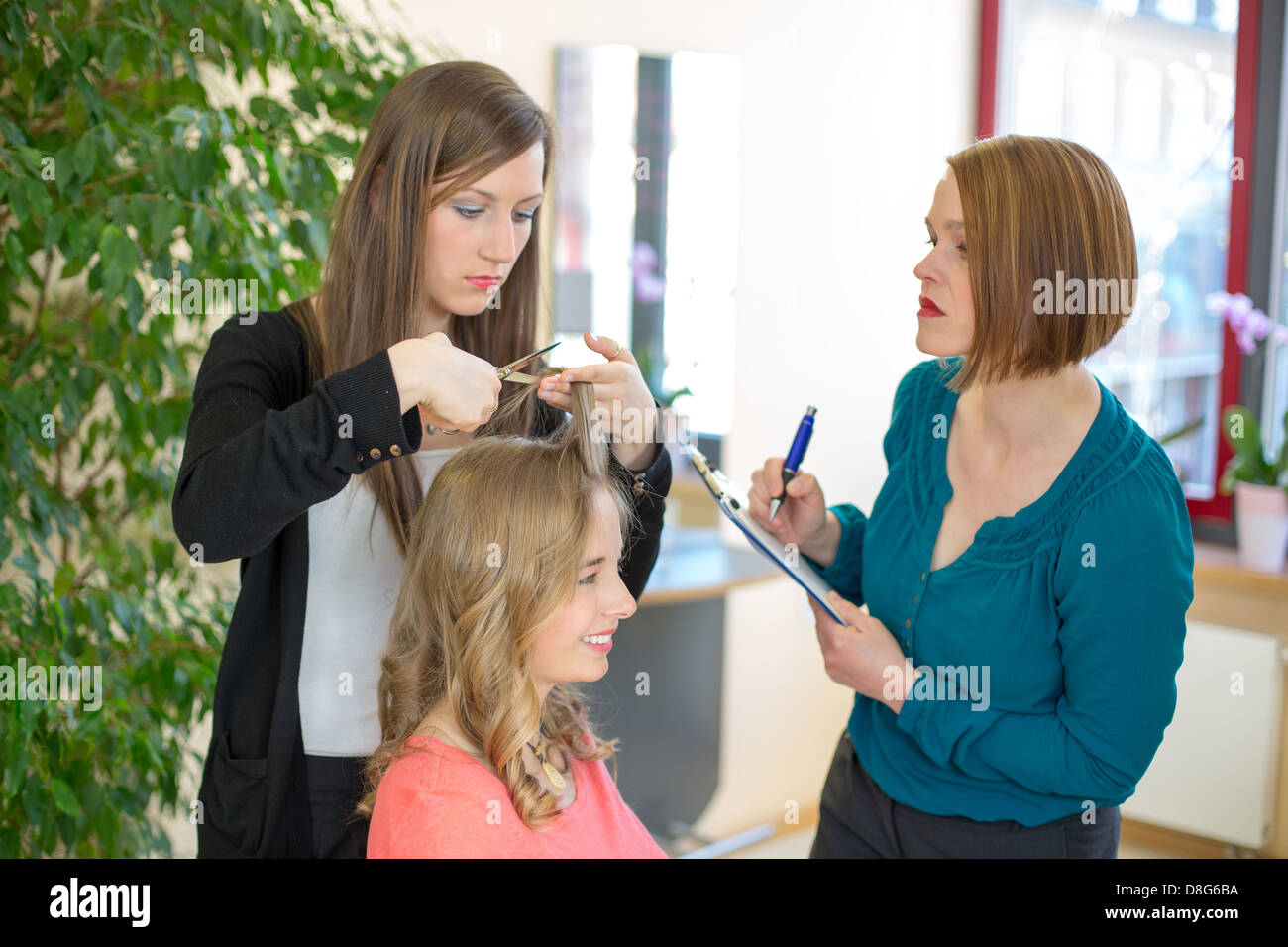 hairdresser apprentice cutting hair while instructor is watching Stock