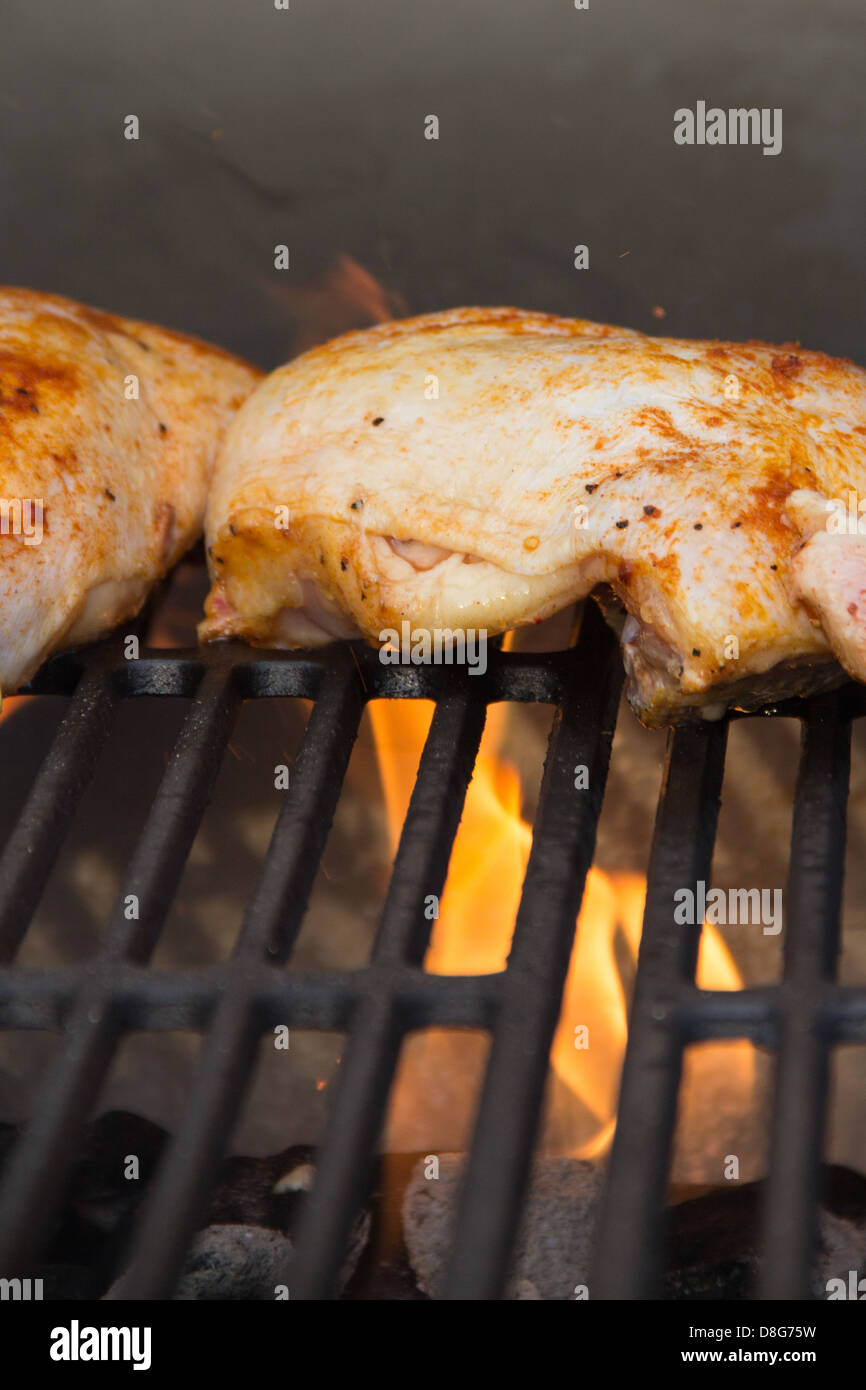 Seasoned chicken legs on a grill with charcoal and flames Stock Photo