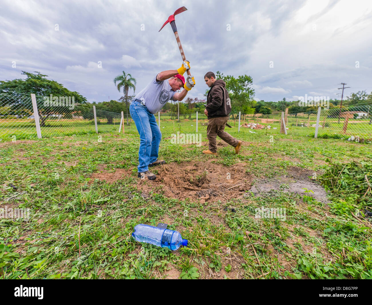 A Caucasian male adult volunteer for Habitat for Humanity Paraguay swings a pick axe high over his head while breaking ground. Stock Photo