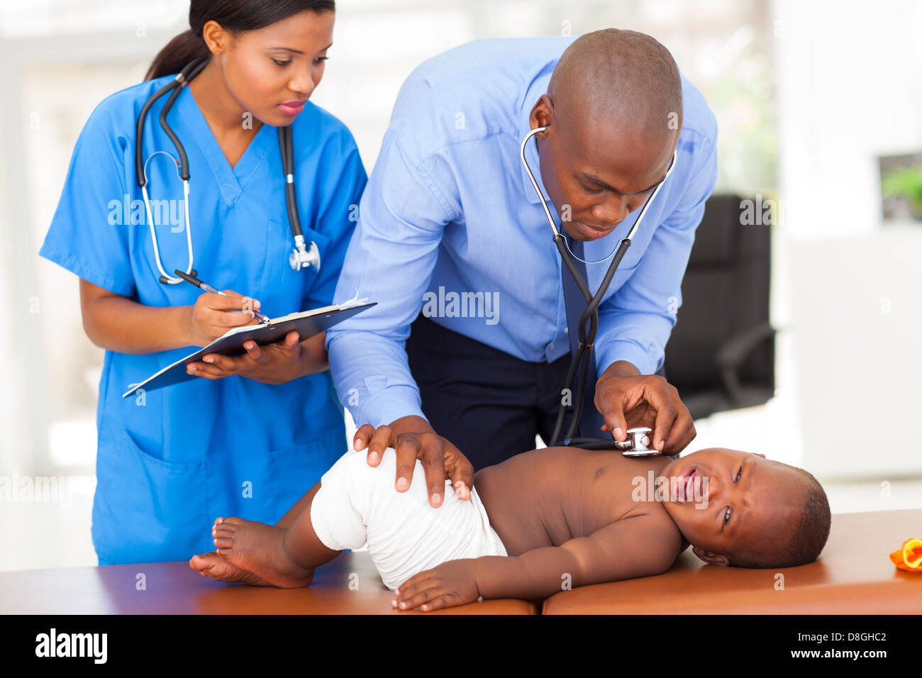 african male pediatrician with nurse assistant examining a child in his office Stock Photo