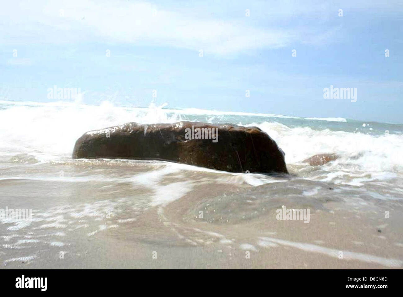 A large rock sits prominently on a beach, surrounded by sand and ocean ...